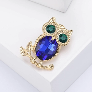 Close-up of golden owl brooch featuring a large blue faceted stone and green gem eyes