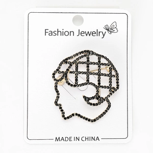 Detailed view of an artistic gold profile brooch with black rhinestones on a white card