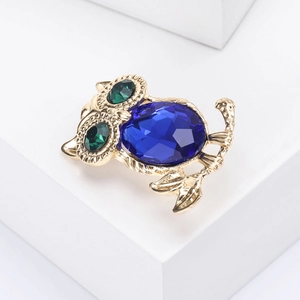 Detailed macro view of owl brooch featuring blue crystal body and green gem eyes on gold