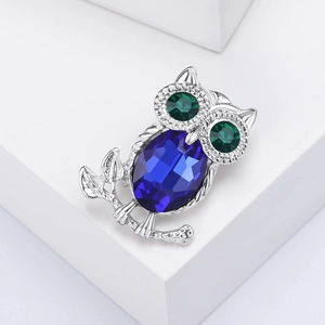 Detailed owl brooch with blue main stone and green eyes on white geometric block