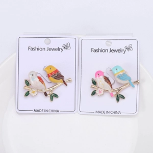 Detailed macro view of two colorful alloy bird brooches on a white ceramic display plate