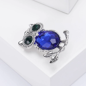 Macro shot of owl brooch detail with navy blue gemstone and green rhinestone eyes