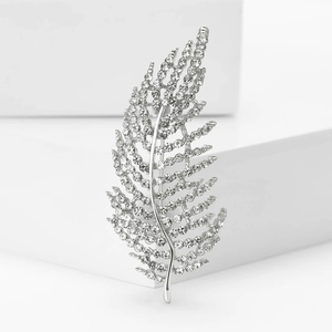 Détail d'une broche feuille argentée avec strass sur des blocs blancs épurés