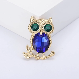 Exquisite gold owl brooch with blue crystal belly and green eyes on white stand