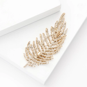 Détail macro de la broche plume dorée avec relief texturé sur un support blanc épuré