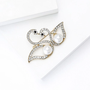 Close-up of golden twin swan brooch featuring radiant pearls and sparkling crystals