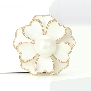 Detalle macro de broche de camelia con perla y bordes dorados en soporte blanco