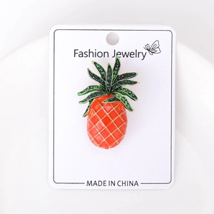 Macro detail of pineapple brooch with orange enamel finish and green rhinestone leaves