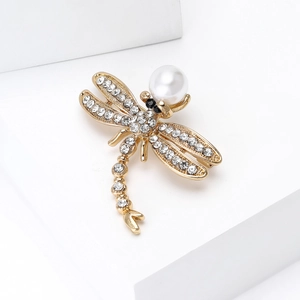 Close-up of gold dragonfly brooch featuring white rhinestones and a single pearl accent