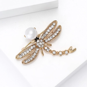 Detailed macro view of dragonfly brooch with gold metal, sparkling crystals and large pearl