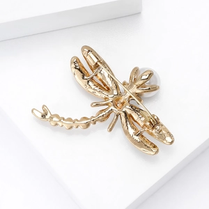 Elegant gold dragonfly brooch with a central pearl inlay on a minimalist white background