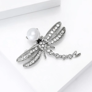 Detailed close-up of a silver dragonfly brooch featuring a large pearl and sparkling rhinestones