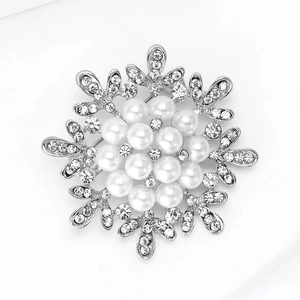 Detailed close-up of a silver snowflake brooch featuring white pearls and sparkling rhinestones