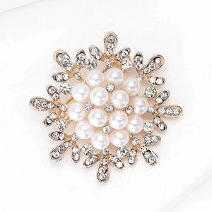 Macro detail of snowflake brooch with gold alloy base, white pearls and sparkling rhinestones