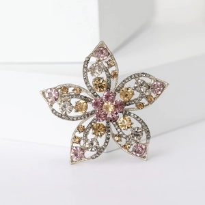 Elegant silver flower brooch with pink and amber rhinestones on a white pedestal