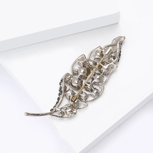 Macro detail of leaf-shaped brooch showing silver alloy base and rhinestone inlay