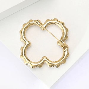 Macro view of golden hollow floral brooch featuring clover design and back pin detail