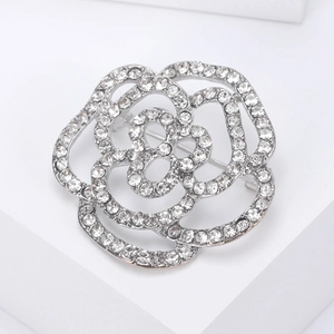 Spilla camelia traforata argento con strass scintillanti su supporto bianco minimale