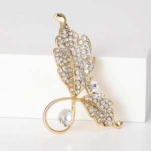 Détail d'une broche feuille dorée ornée de cristaux scintillants et perles sur fond blanc