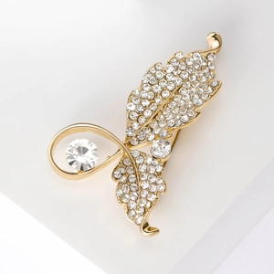 Gros plan d'une broche feuille dorée sertie de zircons blancs sur socle blanc