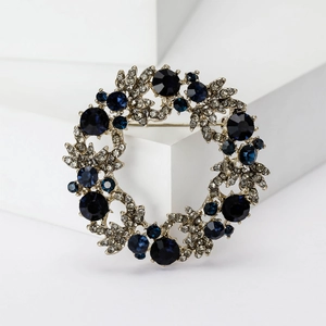 Elegante broche de corona navideña con gemas azul oscuro y diamantes en fondo blanco puro