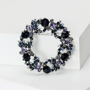 Detalle de un broche de corona con cristales azules y púrpuras en soporte blanco
