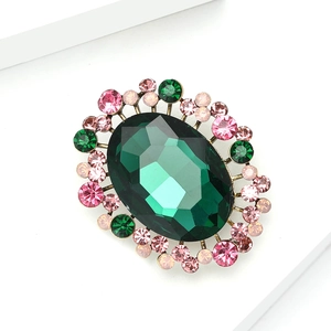 Detail view of a vintage luxury brooch with a deep green oval gem and pink rhinestones