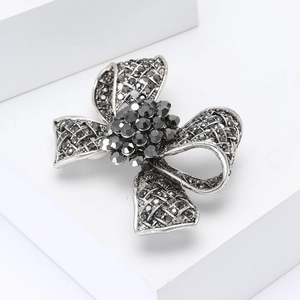 Broche nœud vintage en argent avec strass noirs sur présentoir blanc minimaliste