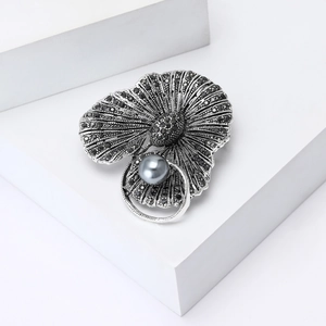 Broche vintage en alliage avec strass noirs et perle grise sur des marches blanches