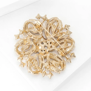 Detail view of the metal safety pin buckle and hollow flower design on a gold brooch
