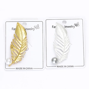 Détail de broches plumes mates dorées et argentées avec perles sur présentoirs