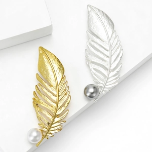 Broches plumes élégantes dorées et argentées avec grandes perles sur socle blanc