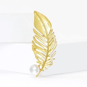 Broche élégante en plume dorée mate avec perle blanche sur support blanc minimaliste