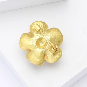 Dettaglio del retro di una spilla a fiore in smalto oro opaco che mostra la chiusura a spillo