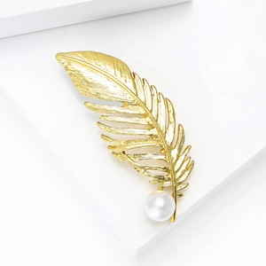 Vue détaillée d'une élégante broche plume dorée avec perle brillante sur bloc blanc