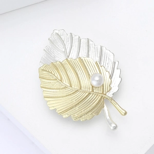 Élégante broche feuille mate or et argent avec perle sur une base blanche minimaliste