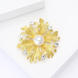 Detail of matte gold floral brooch featuring leaf textures, a center pearl, and zircons