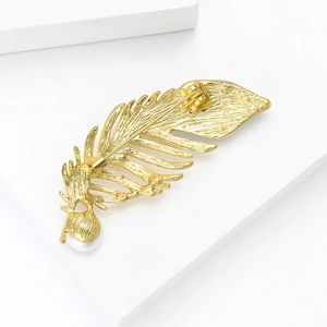Broche plume en or mat avec perle blanche sur un fond géométrique blanc épuré