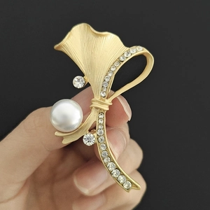 Détail de la broche dorée mate en forme de ginkgo avec grande perle et cristaux scintillants
