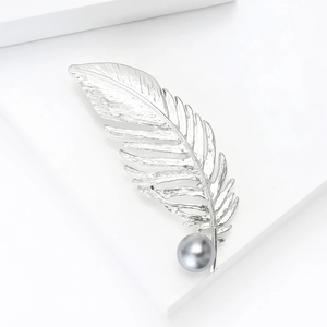 Détail d'une broche plume argentée avec feuilles métalliques et une perle grise
