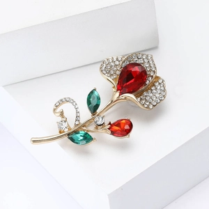 Detailed macro view of an elegant gold rose brooch with red crystals and green leaves