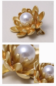 Detail of matte gold floral brooch with a large white pearl center and textured petals