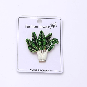 Detail of enamel vegetable brooch with green leaves and sparkling rhinestones on card