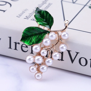 Détail d'une broche raisin dorée élégante avec perles blanches et émail vert fini