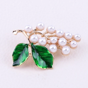 Détail de l'élégante broche dorée avec feuilles en émail vert et perles blanches