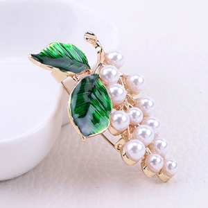 Détail macro d'une broche raisin avec feuilles en émail vert et perles blanches