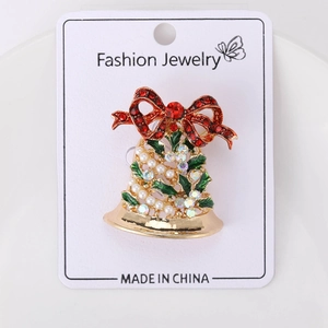Vue détaillée d'une broche cloche de Noël avec strass rouges et feuilles en émail vert