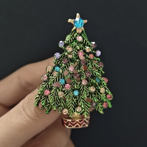 Nahaufnahme der grünen Emaille-Weihnachtsbaum-Brosche mit bunten Strasssteinen in der Hand