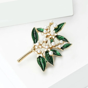 Elegant gold flower brooch with white pearls and green enamel leaves on a white stand