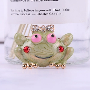 Detailed close-up of a green enamel frog brooch with a gold crystal bow and red rhinestone accents